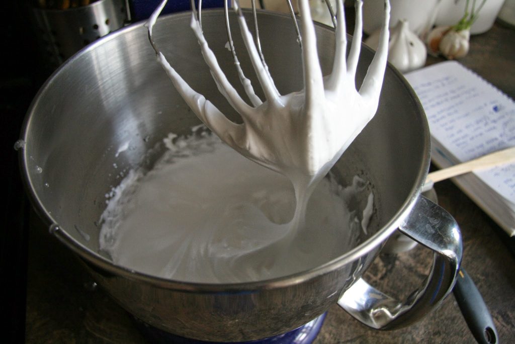 The forming of the Italian meringue after hot syrup is poured into the whisked egg whites. 