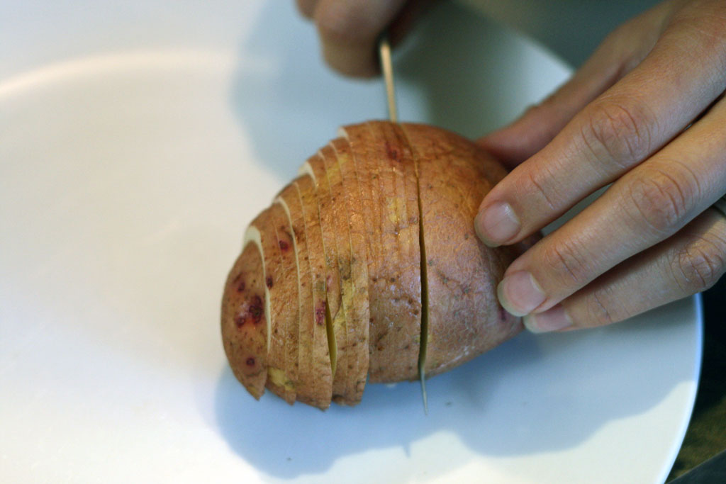 Slicing technique for Hasselback Potatoes. A Potato in the midst of being sliced with a knife.