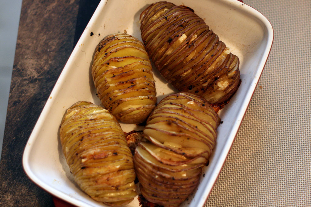 Cooked hasselback potatoes. 4 baked hasselback potatoes in a rectangular servicing dish.