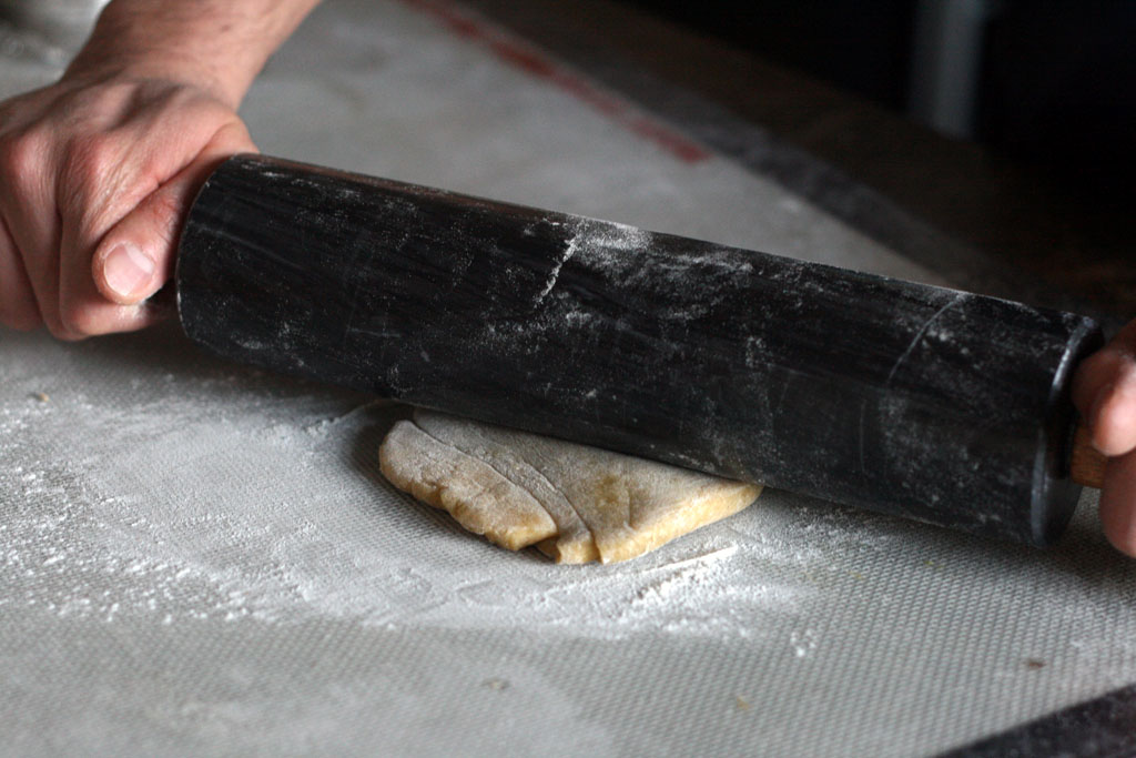 A rolling pin pressed against a flattened disc of dough.