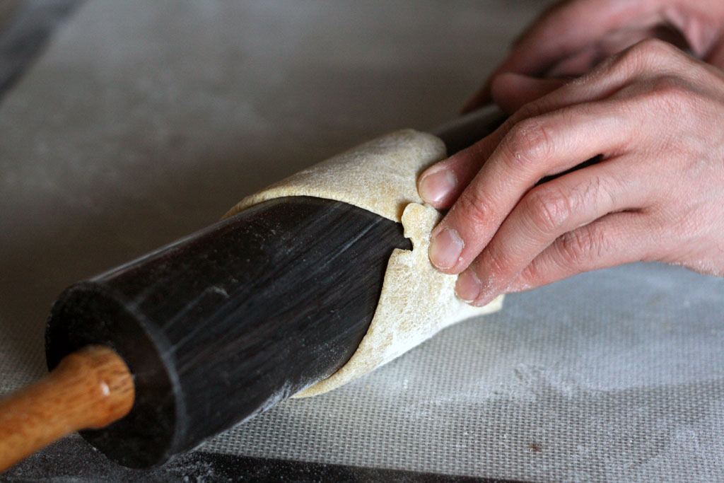 The ends of a flattened dough wrapped around a rolling pin but only slightly overlapping.