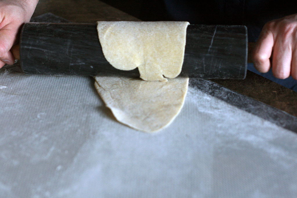 Noodle dough wrapped completely around a rolling pin with enough dough sticking out from under the rolling pin.
