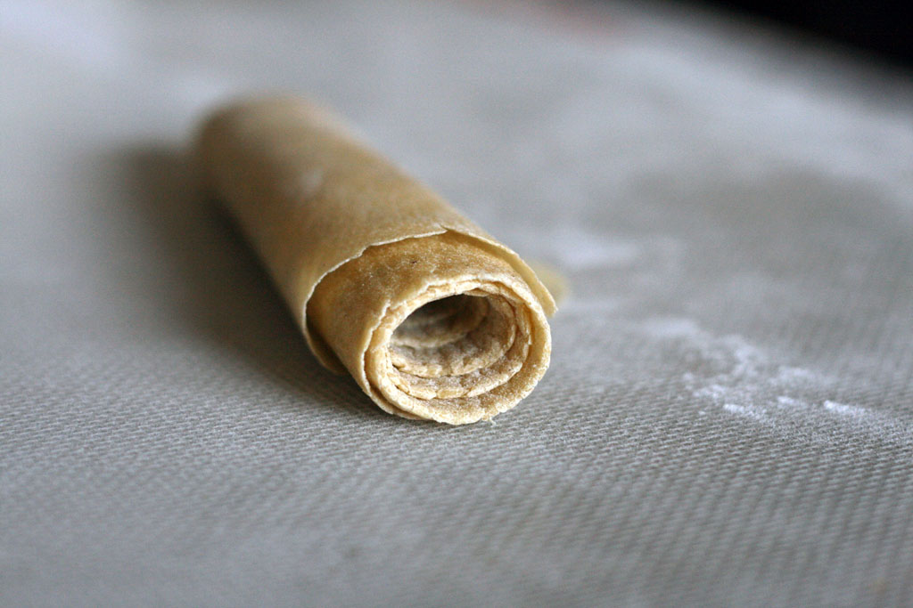 Ramen noodle dough rolled up resting on a floured surface.