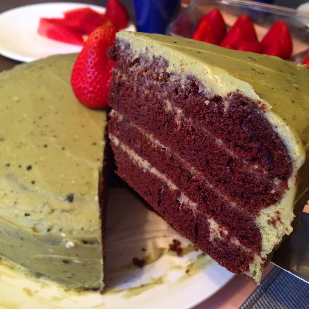 A slice of chocolate cake with matcha buttercream being lifted. The slice shows the four layers of cake with matcha buttercream between each layer.