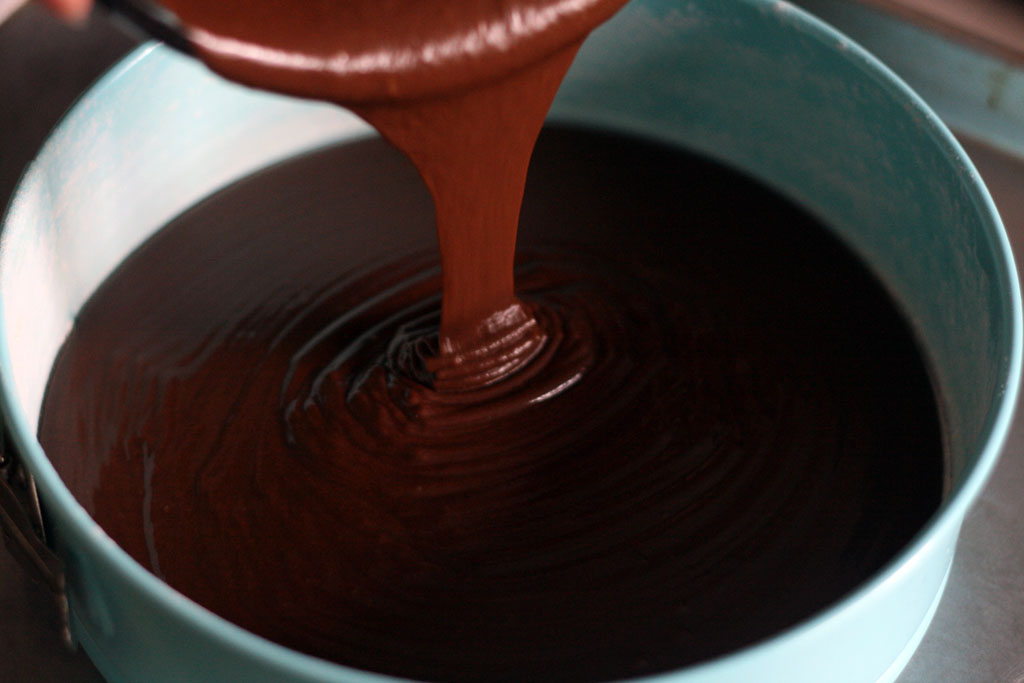 Chocolate cake batter being poured into a blue springform cake pan.