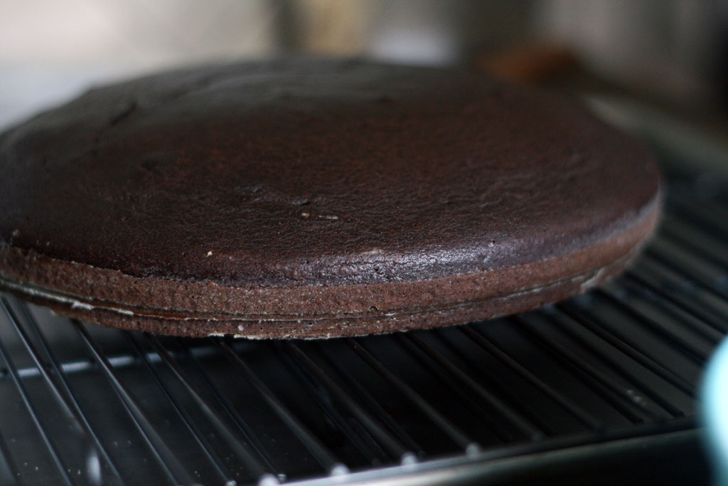 A baked chocolate cake with slight domed top resting on a wire rack.