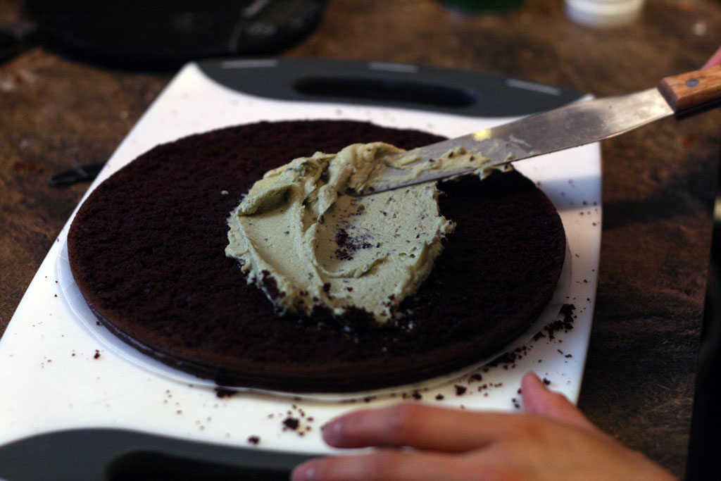 A spatula spreading green tea matcha buttercream on a single layer of chocolate cake.