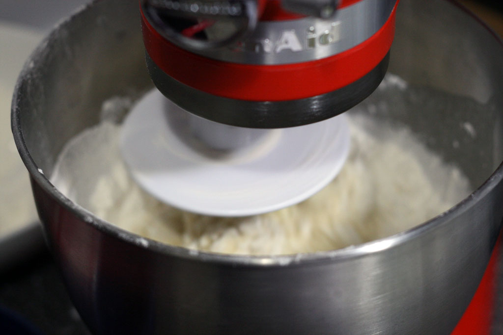 Picture of a red hot kitchen aid turned on and kneading dough in its bowl.