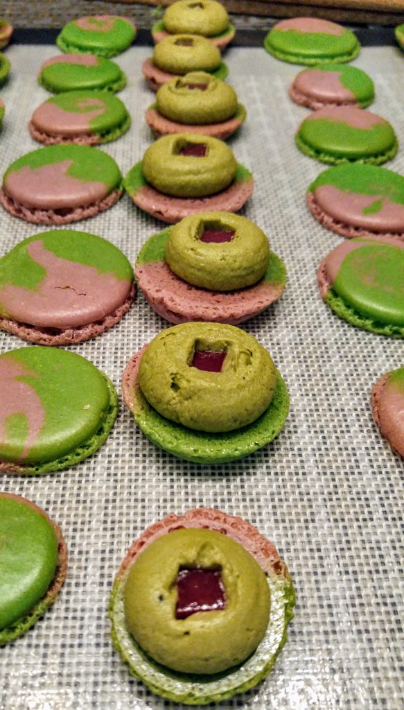 A tray of raspberry matcha macarons with tops separated and raspberry jellies inserted into each filling. 