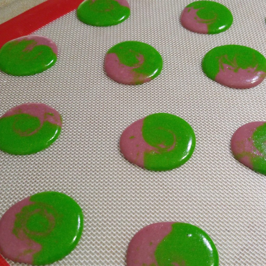 A tray of unbaked marbled raspberry matcha macaron shells. The green shell has sliver of pink macaron batter. 