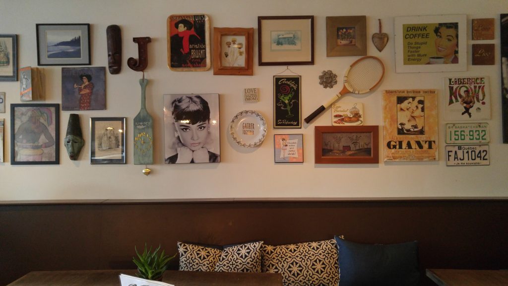 A wall containing various paintings, photos, plates, license plates and knick knacks at Juniper Cafe.