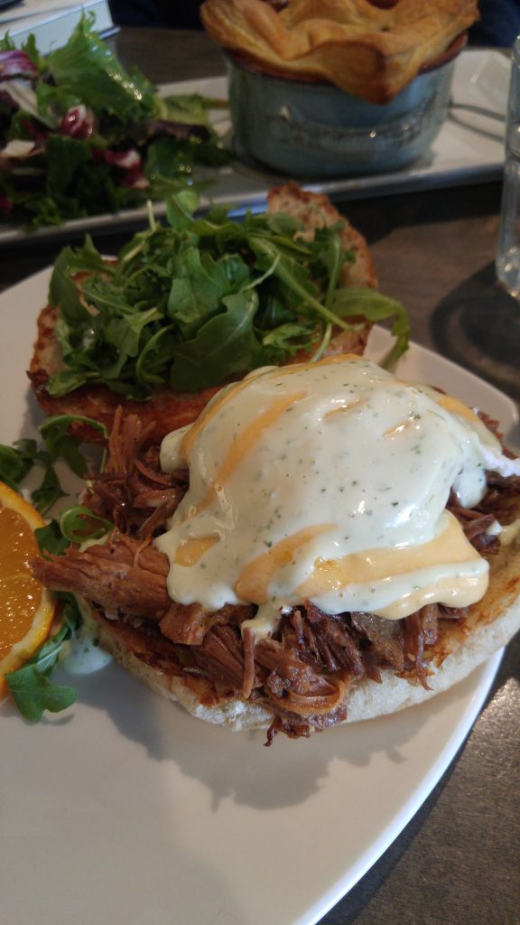 A poached egg benedict sitting on top of pulled pork covered with a white lemon garlic aioli.