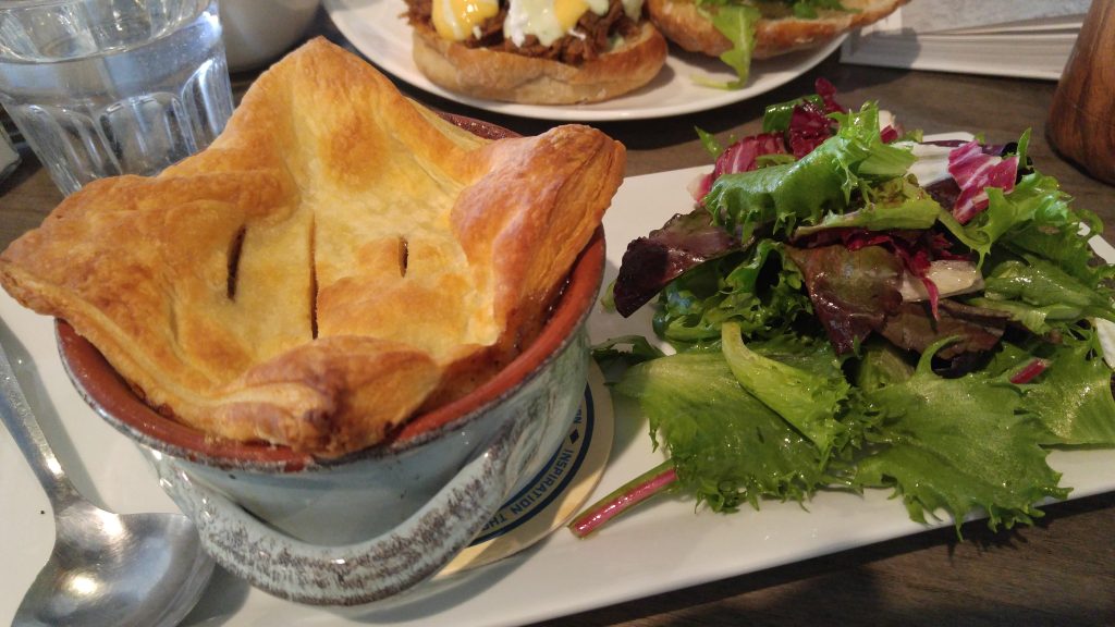 A plate containing a bowl savoury guinness steak and mushroom topped with a flaky pie crust beside a small salad of mixed greens.
