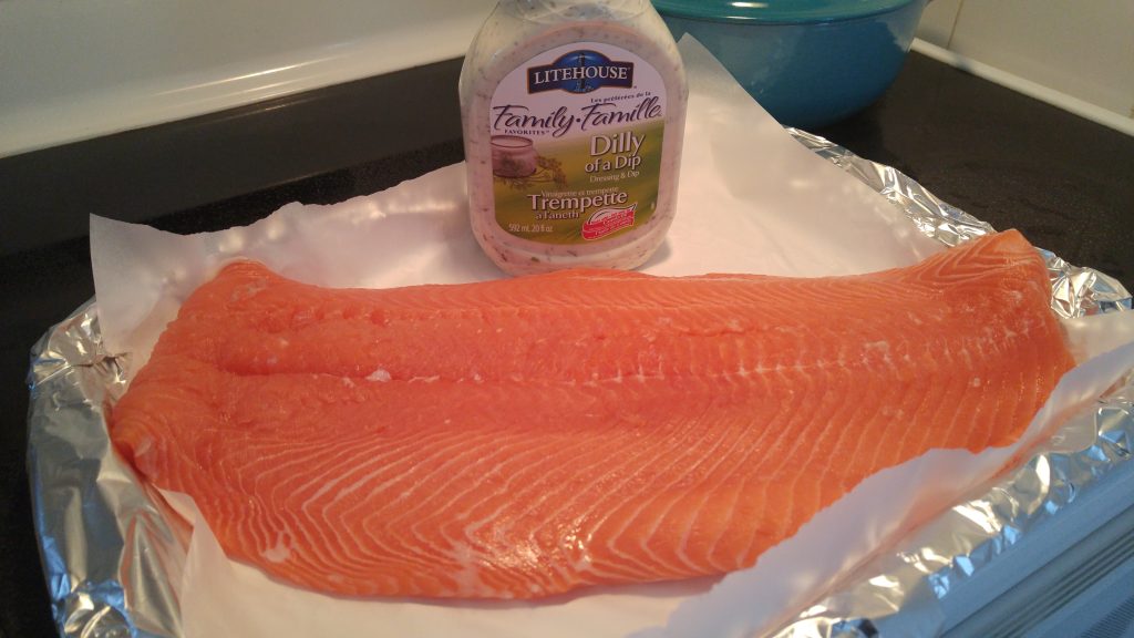 A flank of pink uncooked salmon on a baking tray with a bottle of Litehouse Dilly Dip in the background.