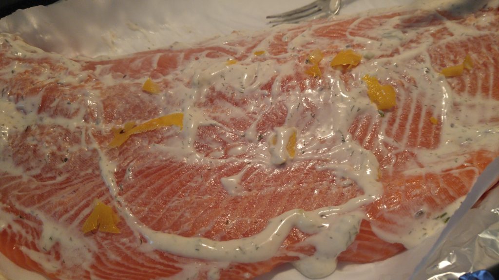 Close up of a filet of salmon with lemon rind slices and covered with white dill dip.
