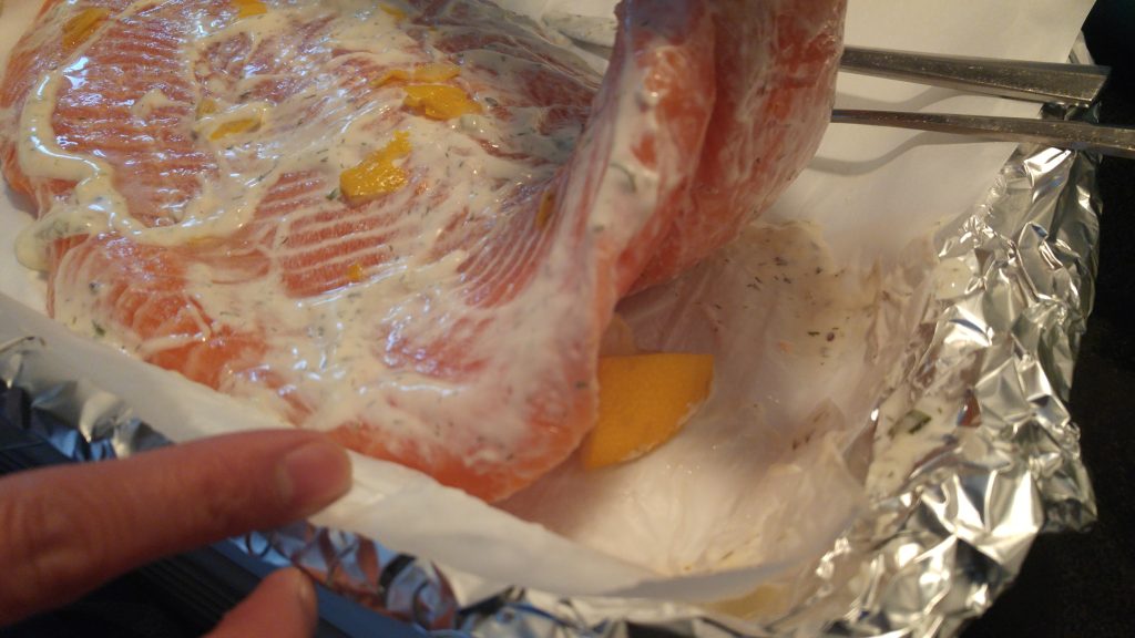 Salmon fillet lifted up to reveal slices of lemon beneath the salmon.