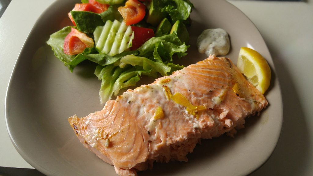 A plate of salmon with dill sauce and salad on the side.