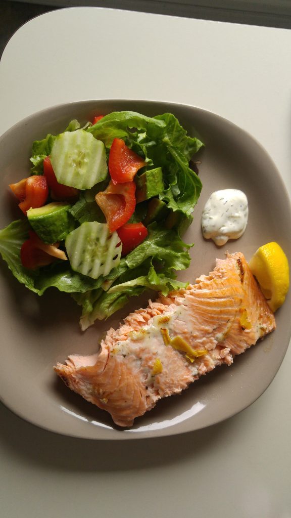 A plate of baked salmon covered with dill dip and lemon zest with salad on the side.