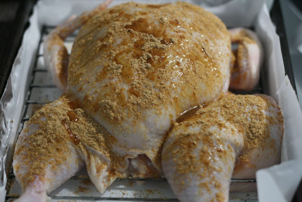 Rubbing the spices all of the chicken which is lying on a grilling rack. It's leg and wings dislocated.