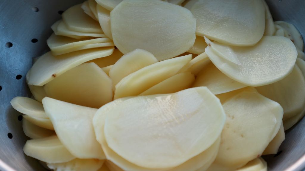 sliced pieces of potato in a metal colander