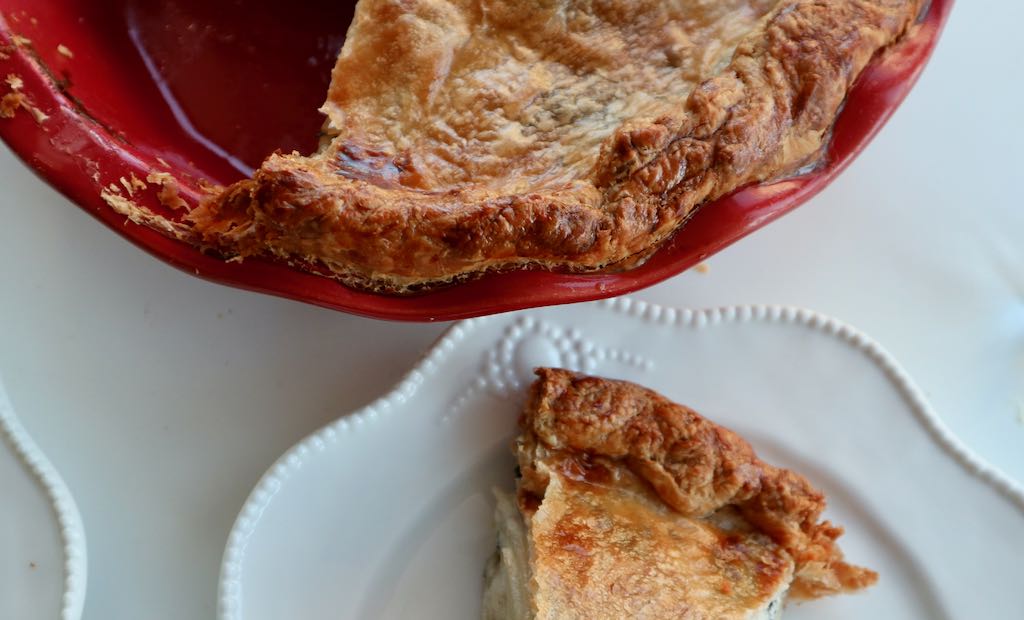piece of potato tourte on a white dish and rest of the potato tourte in a red deep pie dish