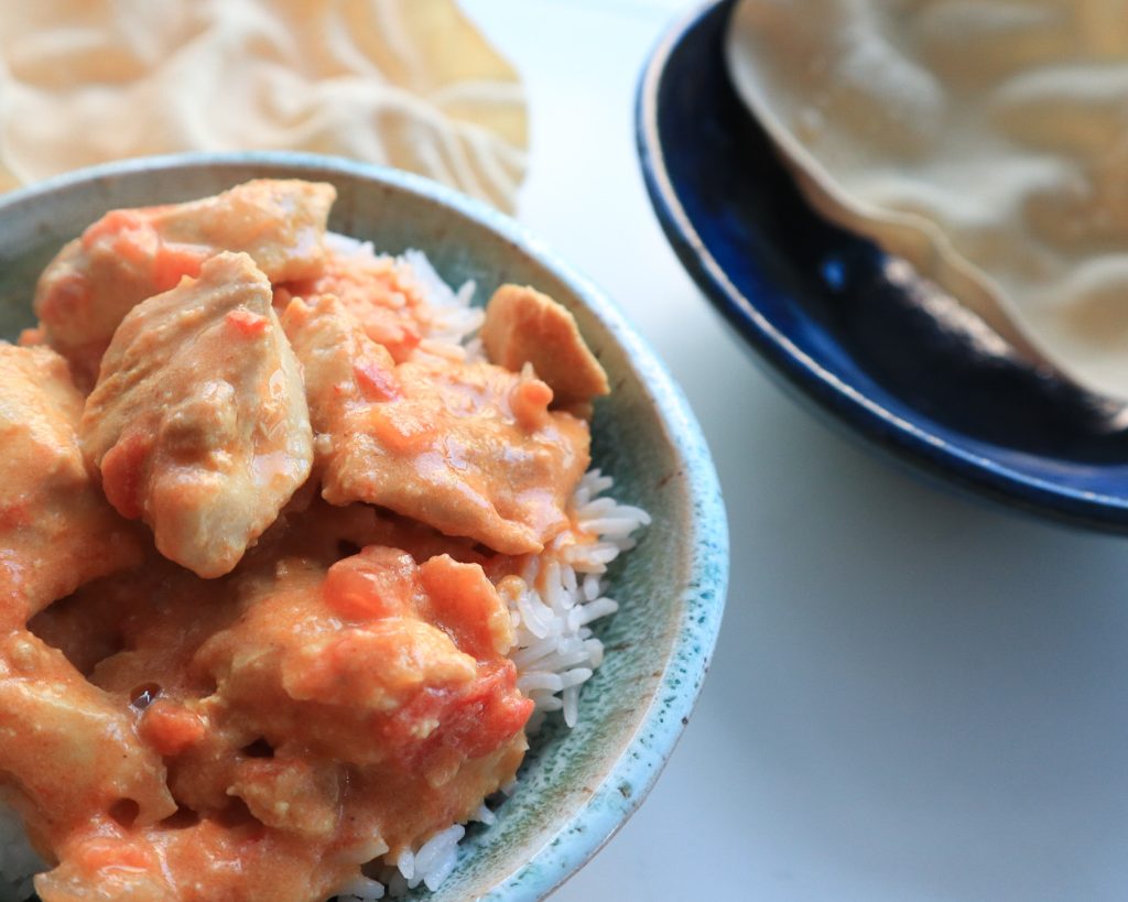 Butter chicken in a bowl with pappadums to the right