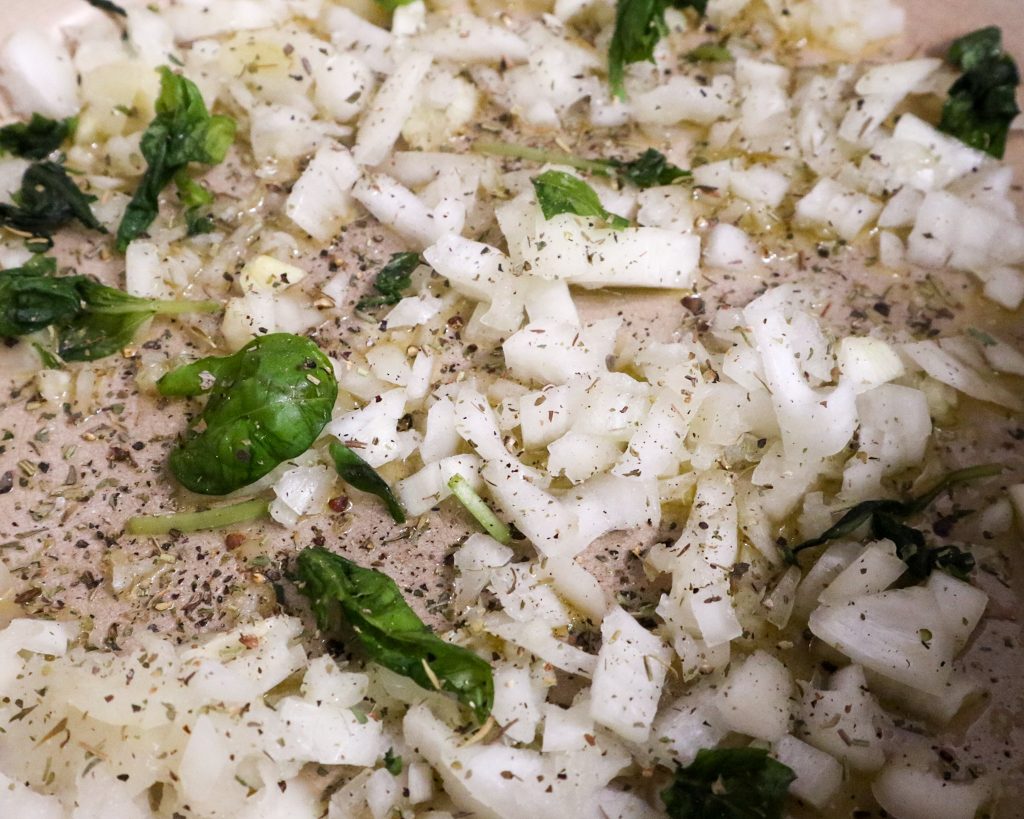 Close up of chopped onions with cracked pepper as the first step to making a vegetable tian.