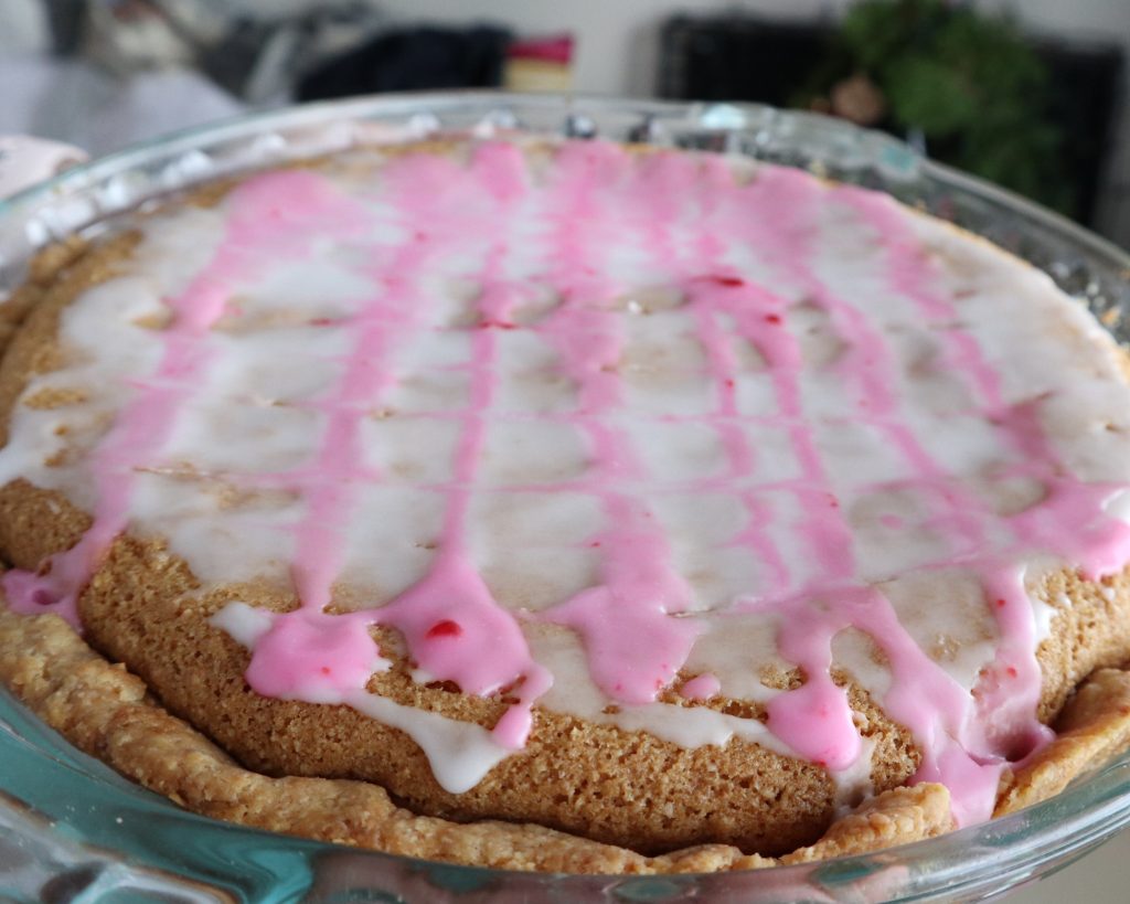 bakewell tart all finished and iced with white icing and feathered lines in pink icing